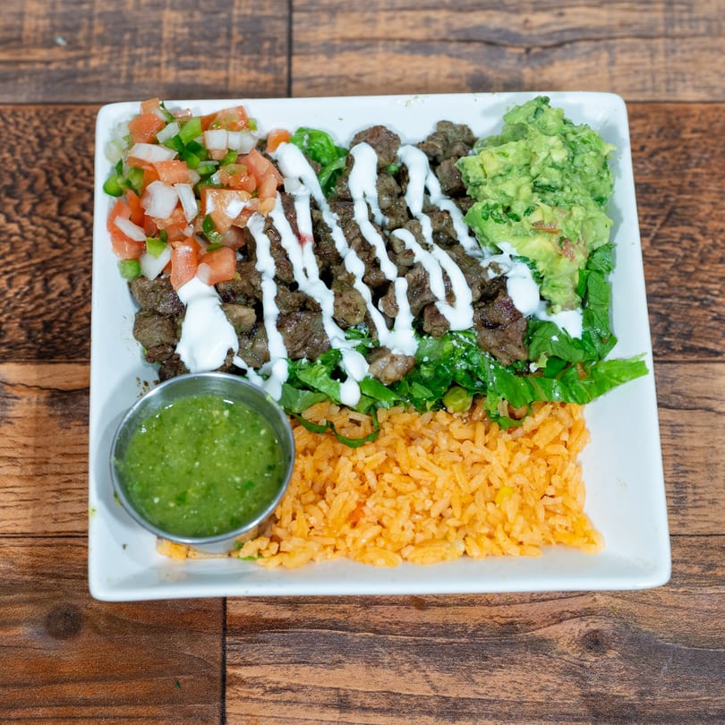 A white rectangular plate with steak, rice, pico de gallo, guacamole, and a side of green salsa.