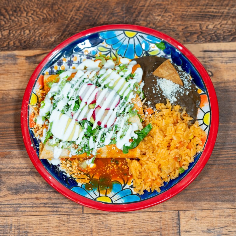 Mexican dish with enchiladas, rice, and refried beans on a colorful plate.