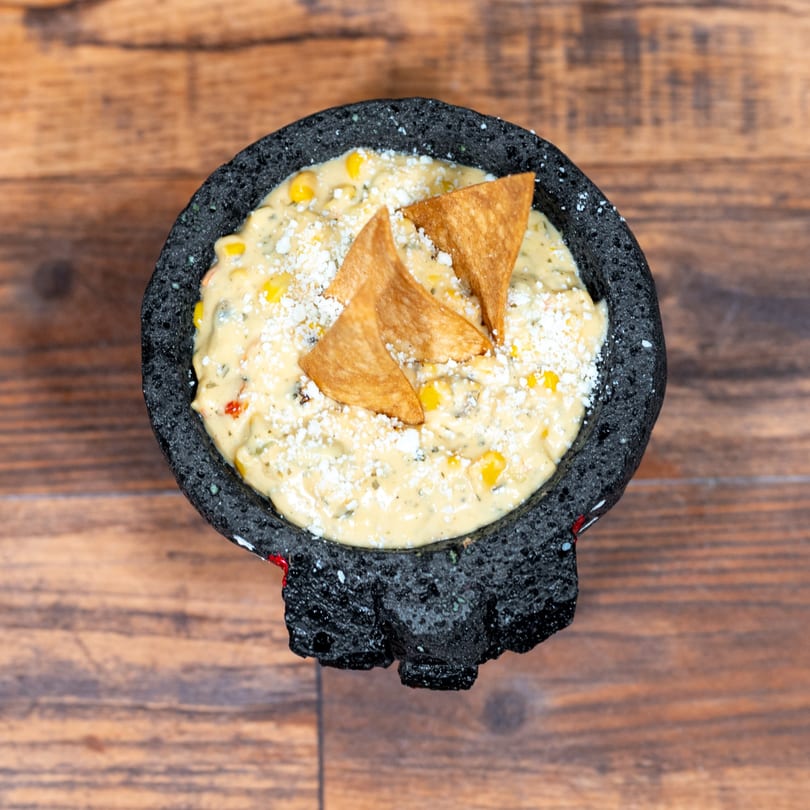 Creamy corn dip with crumbled cheese and tortilla chips in a dark stone bowl on a wooden table.
