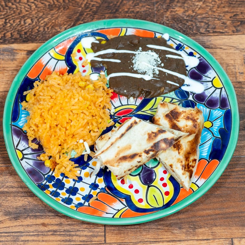 Mexican dish with rice, black beans, and quesadillas on a colorful plate.